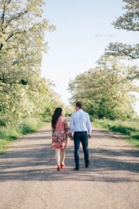 Couple holding hands and walking on road in sunshine among sprin
